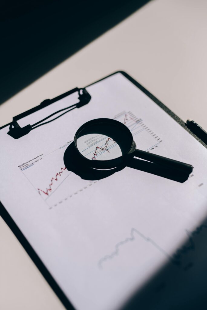 A magnifying glass placed on a clipboard with financial graphs and charts.