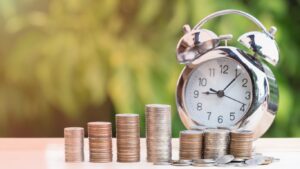 Stacks of coins arranged in ascending order next to a silver alarm clock, symbolizing the importance of timing and financial growth.