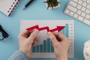 Hands holding a red upward arrow over bar chart, symbolizing business growth and financial resilience, concept for business loans aiding survival during economic downturns.