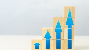 Stacked wooden blocks with ascending blue arrows symbolizing business growth and the importance of working capital for expansion.